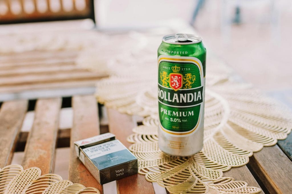 Close-up of Hollandia beer can and cigarette pack on rustic wooden table outdoors.